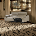 Load image into Gallery viewer, Beige recliner sofa in a living room with patterned rug and curtains.
